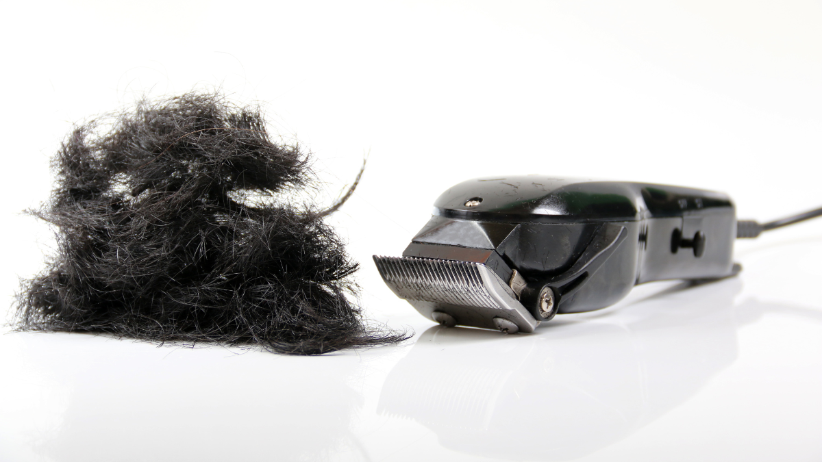 Professional black hair clipper on a white surface with trimmed black hair — premium barber clipper for precise haircuts.